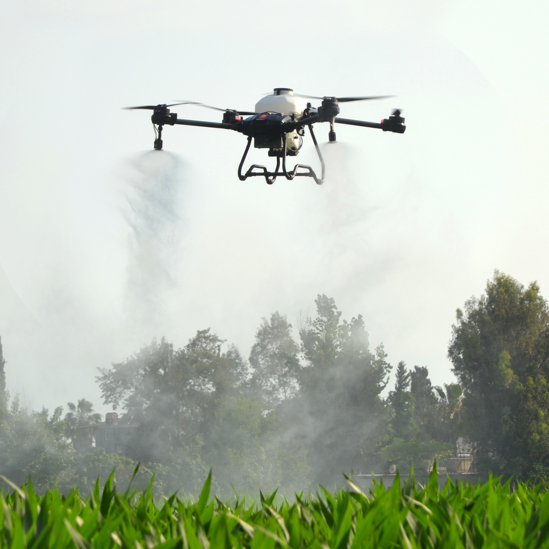 Agricultural spray drone mid-pass over crops with a dense white atomized spray mist plume descending toward the canopy