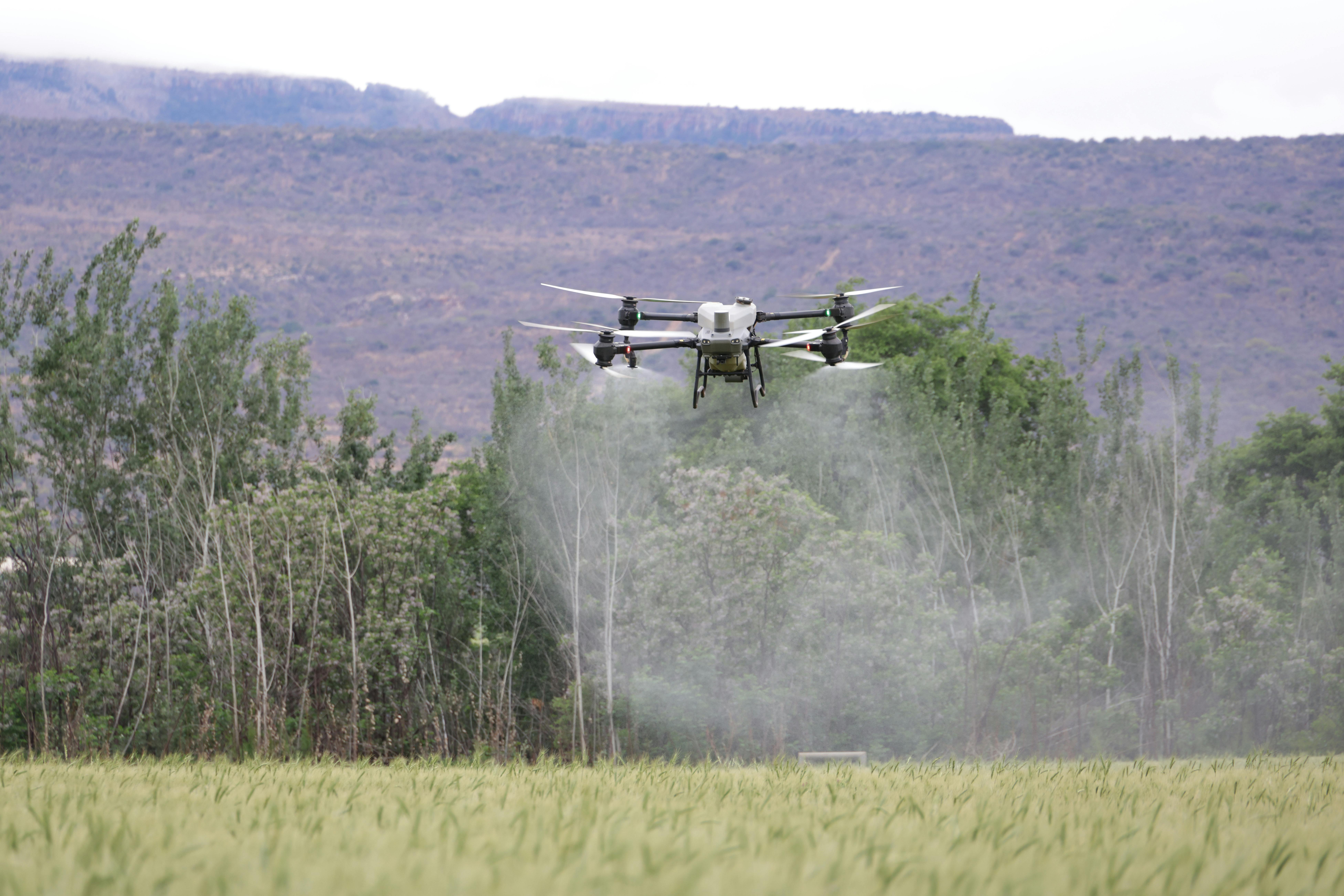 Agricultural spray drone dispersing mist over a wide cultivated field with mountains in the distance