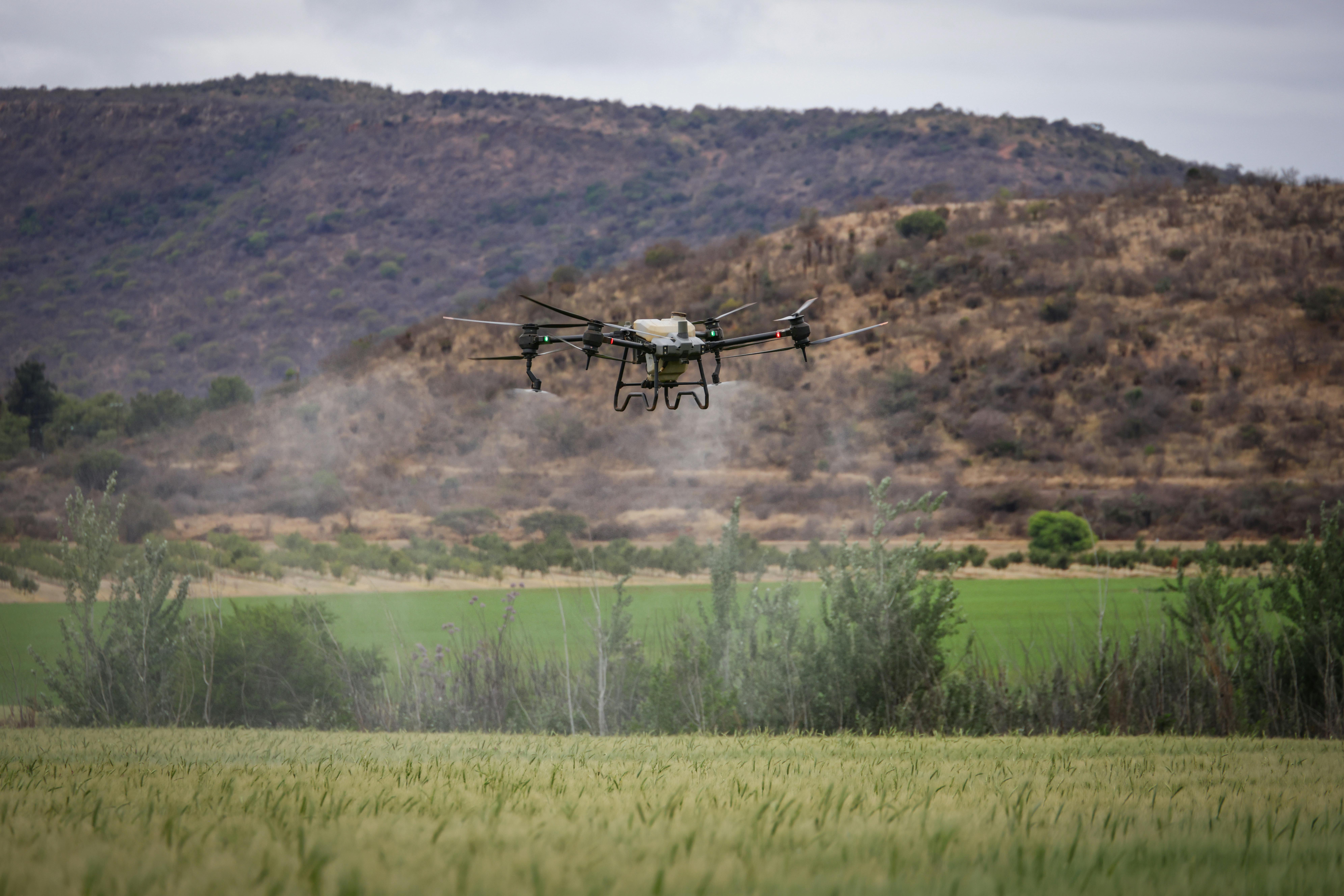 Agricultural drone applying spray over a green field with mountains in the distance