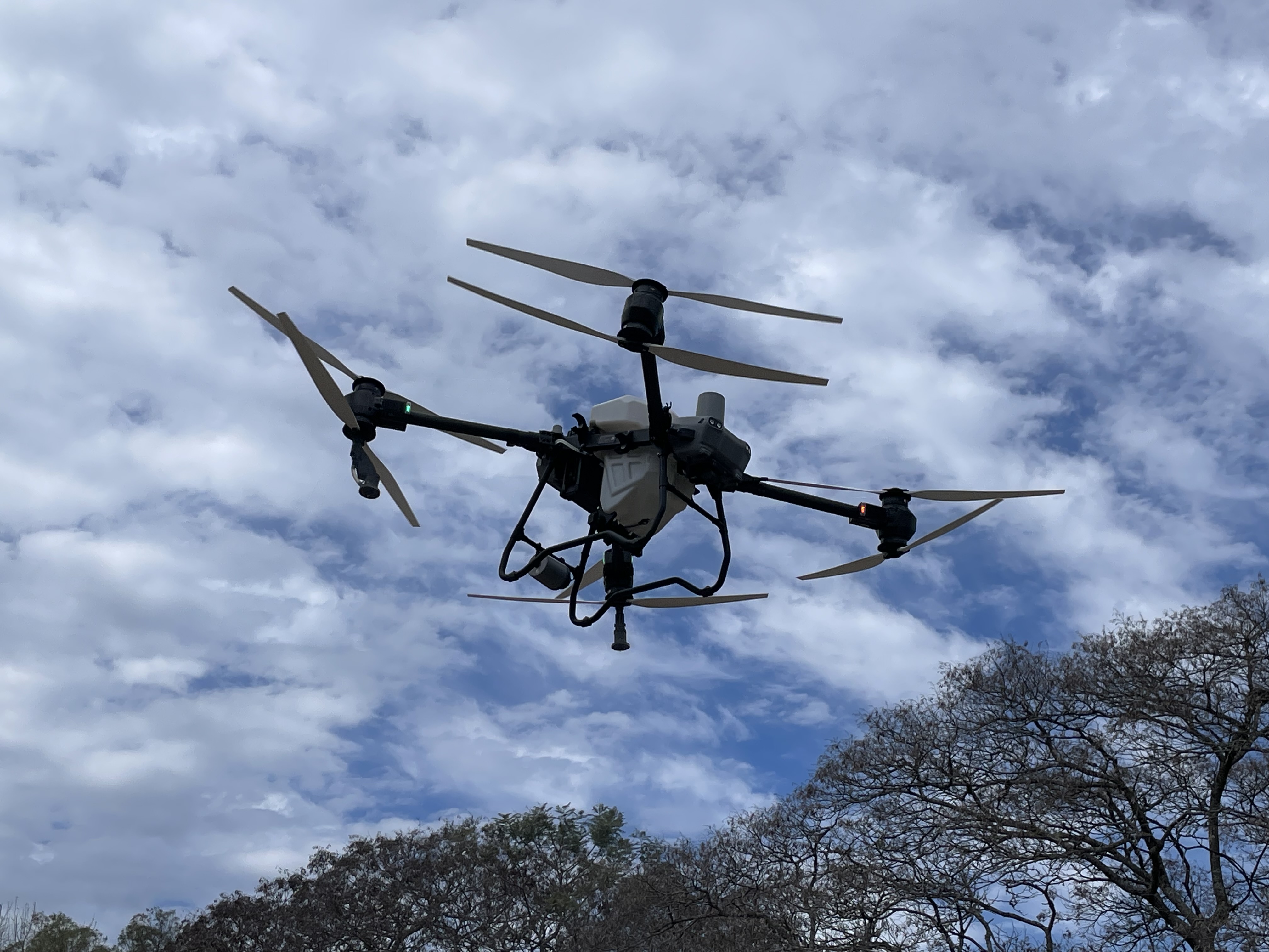 DJI Agras T50 commercial agriculture drone in flight against a cloudy sky