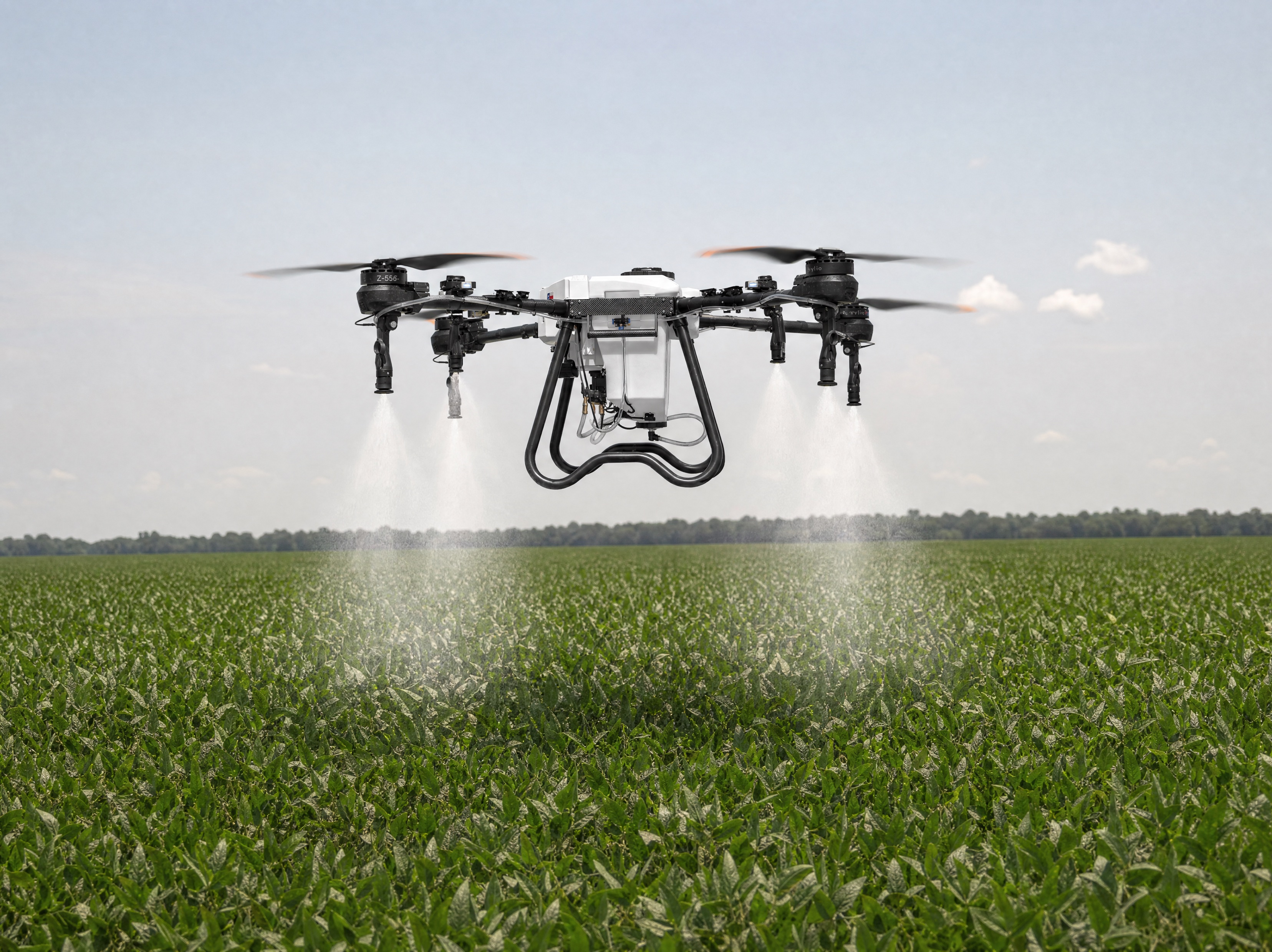 Hylio ARES agricultural drone in active spray over a real soybean field, white atomized mist descending toward the canopy